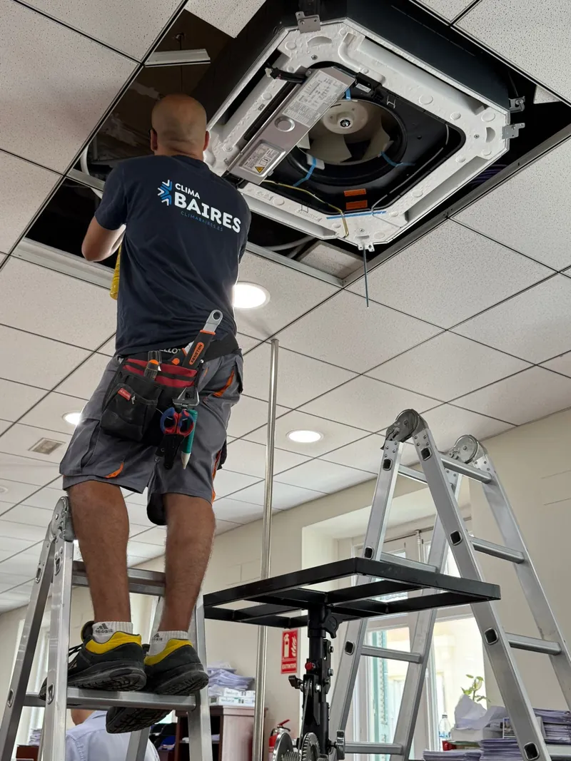 Técnico de Clima Baires fijando una unidad interior tipo cassette en el techo técnico de un local