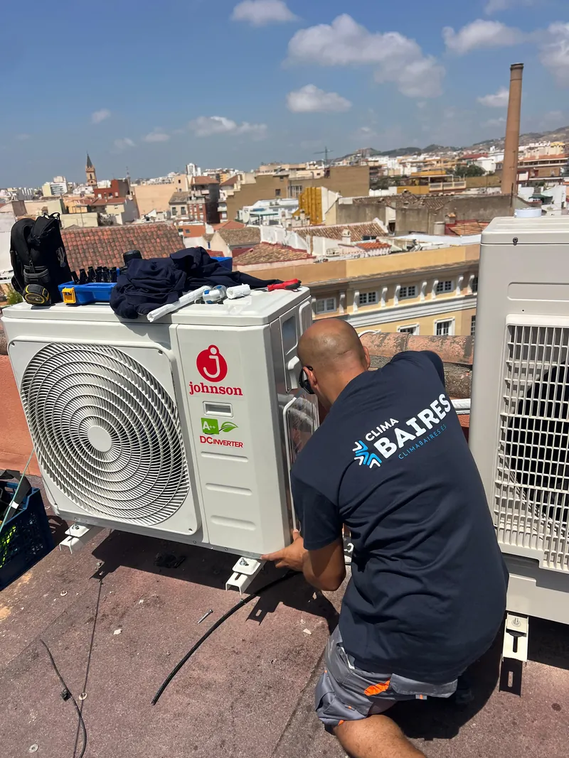 Técnico de Clima Baires montando una unidad exterior inverter en la azotea de un edificio, sobre los tejados de la ciudad